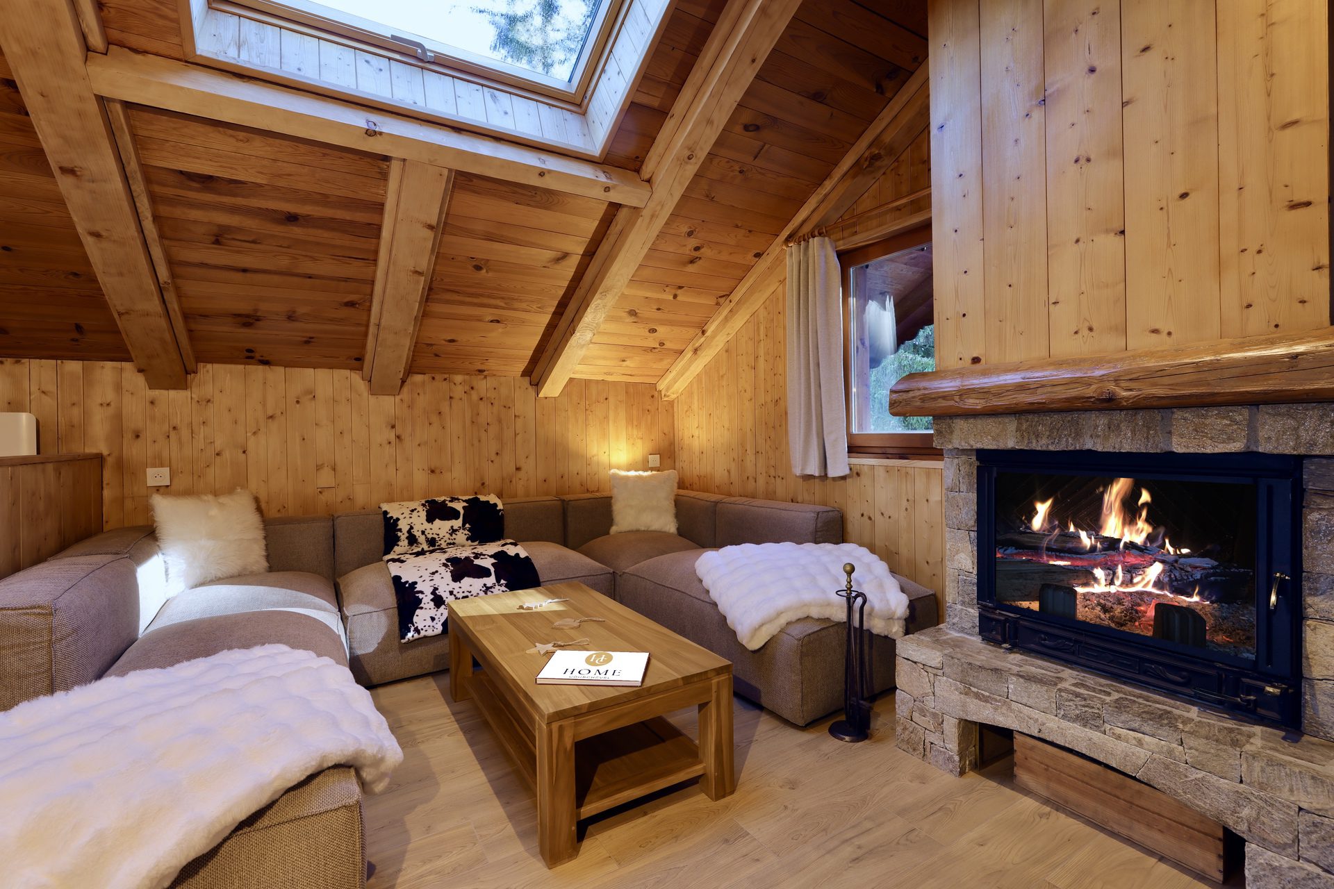Salon cosy du chalet Titania à Courchevel avec cheminée en pierre et charpente en bois